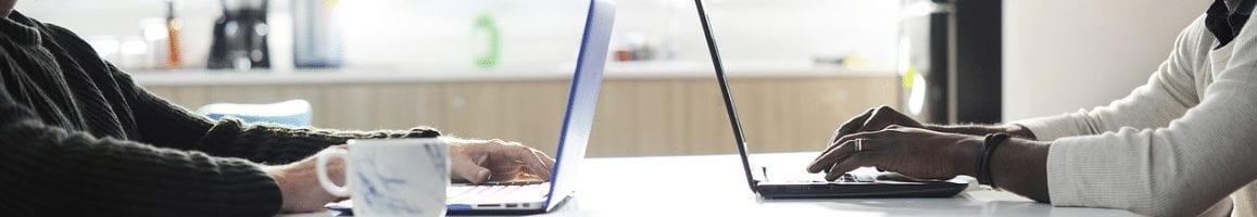 Two employees facing each other working on laptops backed up by cloud servers