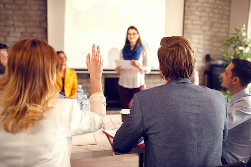 Business person raises hand to make a comment during a presentation. Microsoft is introducing a "Raise Hand" feature for use in Teams meetings.
